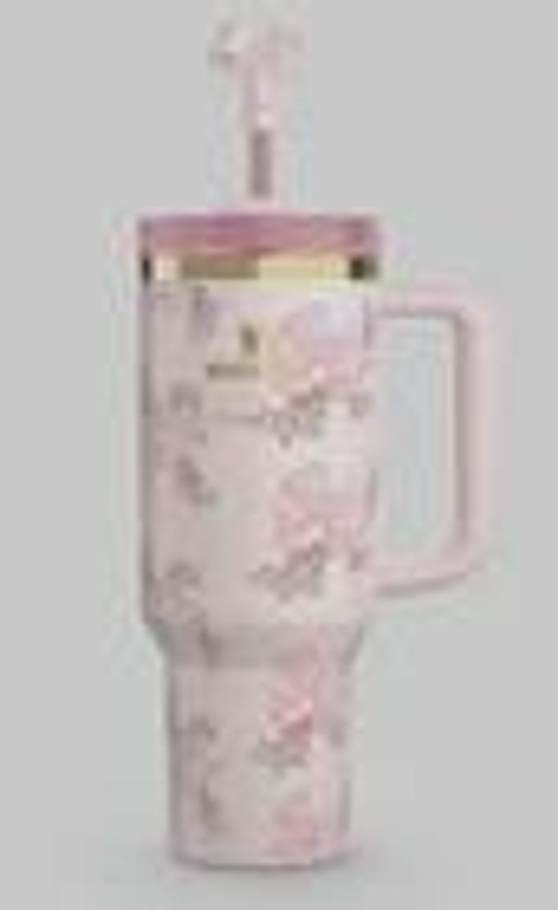 May include: A light pink insulated tumbler with a handle, featuring a repeating pattern of small pink bows. The tumbler includes a matching pink lid with a gold-colored rim and a clear straw. The word Stanley is printed in small letters on the front.