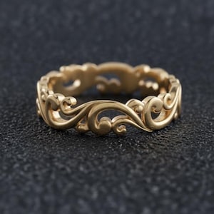 Op de afbeelding: Een goudkleurige ring met een ingewikkeld, doorlopend opengewerkt ontwerp van wervelende, krulachtige patronen die rond de gehele omtrek van de band lopen, wat een gedetailleerde metalen structuur creëert met een gepolijste, reflecterende afwerking.