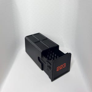 Puede incluir: Una caja rectangular negra con un cajón extraíble. La cara del cajón tiene el número "223" en rojo. La parte superior de la caja tiene una serie de líneas paralelas. El cajón está parcialmente abierto.