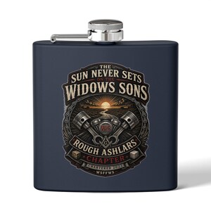 Puede incluir: Una petaca de metal azul marino mate con tapa de rosca plateada. El frente presenta un gráfico con dos pistones, un sol y el texto: The Sun Never Sets On The Widows Sons, Rough Ashlars Chapter, Chartered 2023, WSFFWS y WS.