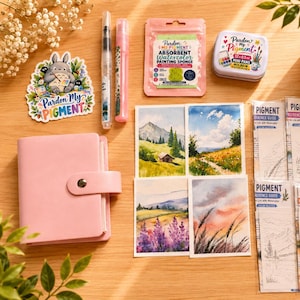 May include: A watercolour painting kit featuring a pink binder, a sticker with a cartoon character, a sponge in a pink pouch, a metal tin of mini watercolour pans, and several reference guide cards depicting landscape scenes and line drawings.