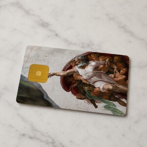 May include: A rectangular card featuring a portion of Michelangelo's 'The Creation of Adam' fresco. The card has a gold square chip on the left side. The artwork depicts a bearded figure reaching out to touch another figure.