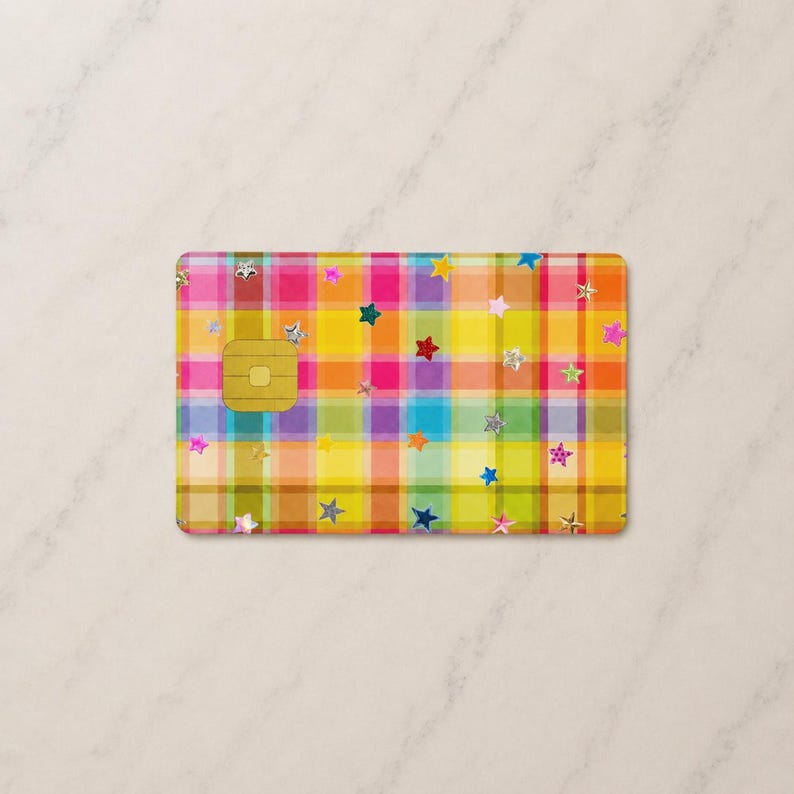 Peut inclure: Une carte de cr&eacute;dit rectangulaire pr&eacute;sentant un motif &agrave; carreaux multicolore vif dans des tons de jaune, rose, orange et bleu. La surface est d&eacute;cor&eacute;e de nombreuses petites &eacute;toiles dispers&eacute;es de diff&eacute;rentes couleurs et d'une puce EMV dor&eacute;e.