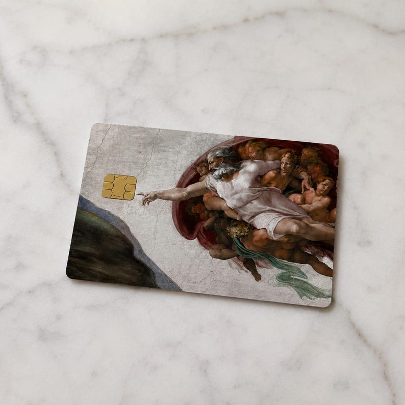 May include: A rectangular credit card featuring a reproduction of Michelangelo's "The Creation of Adam" fresco. The card has a gold-colored EMV chip on the left side. The artwork depicts God reaching out to Adam.