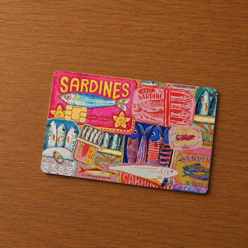 May include: A colorful rectangular sardine-themed design with the word "SARDINES" in large pink letters. The design features illustrations of sardines, cans, and labels, with text including "IN OLIVE OIL".