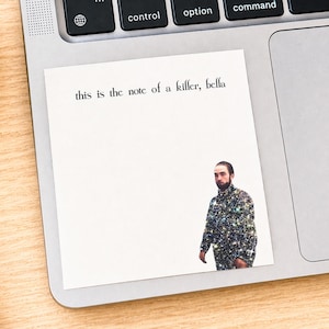 May include: A white sticky note with the text "this is the note of a killer, bella" in black. A man in a sparkly jacket is pictured on the bottom right corner of the note. The note is on a laptop.