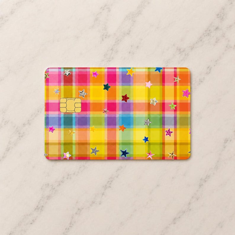 Peut inclure: Une protection de carte bancaire rectangulaire arborant un motif &agrave; carreaux multicolore vif dans des tons de jaune, orange, rose, bleu et vert. La surface est d&eacute;cor&eacute;e de nombreuses petites &eacute;toiles dispers&eacute;es de diff&eacute;rentes couleurs et finitions.