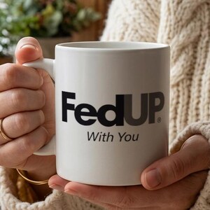 以下が含まれることがあります： 前面に黒い文字でFedUP、その下に小さく黒い文字でWith Youとプリントされた白いセラミック製のマグカップ。標準的な持ち手が付いた滑らかな質感のマグカップで、ニュートラルでぼやけた背景を前に両手で持たれている。