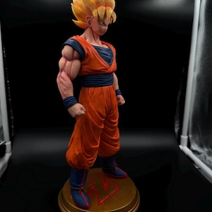May include: A detailed figurine of a character from the Dragon Ball series. The figure is in a dynamic pose, wearing an orange and blue outfit with spiky yellow hair. The base is gold with a red symbol.