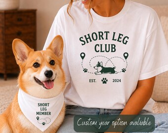 May include: A white t-shirt featuring the dark green text SHORT LEG CLUB, a graphic of a corgi, paw prints, and location markers with the text EST. 2024. A white pet bandana with the text SHORT LEG MEMBER, a location marker, and a paw print graphic.