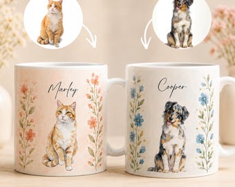 May include: Two white ceramic mugs with custom pet portraits. One mug features a cat named Marley, the other a dog named Cooper. Floral and leaf designs surround the portraits. The mugs are white with a handle.