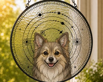 May include: A circular stained glass suncatcher featuring a detailed illustration of a long-haired dog with tan and brown fur. The dog is centered against a background of celestial orbits, stars, and planets, all enclosed in a black metal frame.