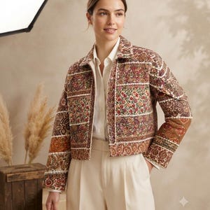 Puede incluir: Una chaqueta corta con un patrón de patchwork floral y de cachemira multicolor en tonos rojos, naranjas y marrones. La chaqueta tiene un cuello clásico, mangas largas y cierre de cremallera frontal, sobre una camisa blanca de botones.