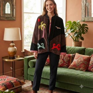 May include: A long-sleeved jacket featuring a colour-blocked design in brown and black. The jacket is decorated with embroidered patches including a palm tree, a red sun, a bird, and stylised wave patterns in teal and red on the front panels.