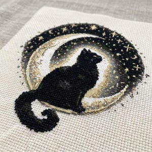 Könnte beinhalten: Kreuzstichmuster mit einer schwarzen Katzen-Silhouette vor einem Halbmond und Sternen. Der Mond ist eine Mischung aus Weiß, Gold und Grau, mit einem dunklen Sternenhintergrund. Der Schwanz der Katze ist zur Seite gerollt.
