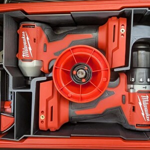 Op de afbeelding: Een rode en zwarte Milwaukee gereedschapsset, netjes georganiseerd in een rode koffer. De set bevat een boor, slagschroevendraaier en batterij, allemaal gerangschikt in op maat gemaakte compartimenten. De gereedschappen zijn voorzien van het merk Milwaukee.