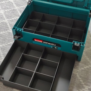 May include: An open teal and gray tool organizer with multiple compartments. The organizer has a pull-out drawer with additional storage. The brand name "Makita" and model "DDF484RTJ" are visible on the front.