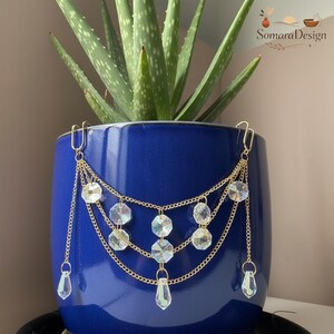 May include: A gold-colored plant pot chain with clear, iridescent crystals. The chain hangs from a blue ceramic pot holding a green aloe vera plant. The crystals are various shapes, including round and teardrop. The pot has a glossy finish.