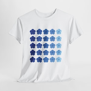 Könnte beinhalten: Weißes T-Shirt mit einem Rastermuster aus blauen Blumenmotiven. Die Blumen sind in verschiedenen Blautönen gehalten, wodurch ein Farbverlauf entsteht. Das Shirt besteht aus einem weichen, leichten Material, das sich für den Alltag eignet.