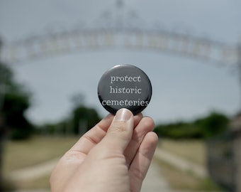 Op de afbeelding: Een ronde zwarte button met de witte tekst "protect historic cemeteries" in het midden aan de voorzijde. De button heeft een gladde, glanzende afwerking en een eenvoudig, strak ontwerp met duidelijke, leesbare letters op de donkere achtergrond.