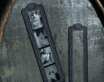 Op de afbeelding: Een verticale zwarte lijst met sierlijke, gotisch geïnspireerde krulwerkranden en een klein schedelpictogram aan de bovenkant. De lijst bevat een strook van vier zwart-witfoto's die een kat in verschillende houdingen tonen tegen een grijze, getextureerde achtergrond.