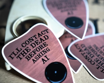 Op de afbeelding: Een set hartvormige stickers met een houtnerfpatroon, elk voorzien van een zwarte cirkelvormige uitsparing en de gedrukte tekst: I'LL CONTACT THE DEAD BEFORE ASKING AI. De stickers zijn gestapeld om het ontwerp duidelijk weer te geven.