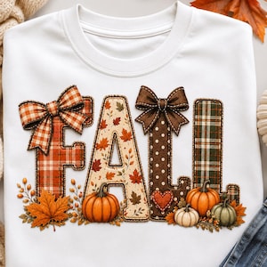 May include: A white crewneck sweatshirt featuring the word FALL in large, decorative letters. The letters are adorned with orange plaid, autumn leaf patterns, brown polka dots, and green plaid, accented by brown bows, pumpkins, and leaves.