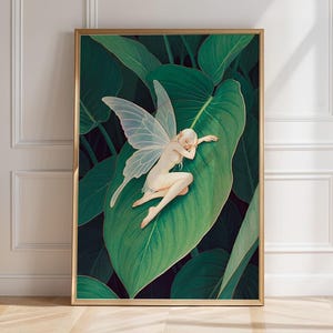 Op de afbeelding: Een ingelijste rechthoekige wandkunstprint met een bleke, gevleugelde feeënfiguur die rust op een groot, levendig groen blad. Het kunstwerk is geplaatst tegen een donkere, schaduwrijke achtergrond van dicht gebladerte, wat het contrast tussen de lichte figuur en de bladeren benadrukt.