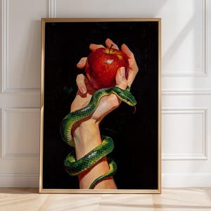 Peut inclure: Une impression d'art mural verticale encadrée représentant une peinture réaliste d'une main tenant une pomme rouge vif avec un serpent vert enroulé autour du poignet et de l'avant-bras, sur fond noir dans un cadre fin de couleur dorée.