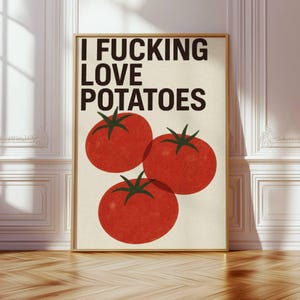 May include: A rectangular wall art print in a light wood frame featuring the black text I FUCKING LOVE POTATOES at the top. Below the text are three large, round, red tomatoes with green stems, illustrated in a flat, graphic style on a cream background.