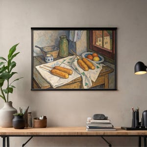 May include: A framed print of a still life painting featuring corndogs on a white cloth, a green pitcher, and a bowl of fruit. The scene is set on a wooden table near a window with a view of buildings. The artwork has a vintage aesthetic.