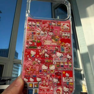 May include: Clear phone case with a pink interior featuring a collage of Hello Kitty characters and holiday-themed graphics. The case includes text that reads "Hello Kitty," "Merry Christmas," and "45th Anniversary."