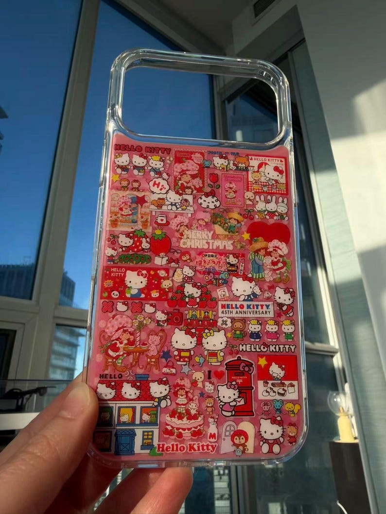 May include: Clear phone case with a pink interior featuring a collage of Hello Kitty characters and holiday-themed graphics. The case includes text that reads "Hello Kitty," "Merry Christmas," and "45th Anniversary."