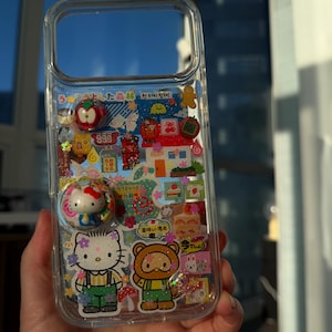 Puede incluir: Funda de tel&eacute;fono transparente decorada con pegatinas y abalorios de colores. Presenta a Hello Kitty, un oso y otras ilustraciones bonitas. Incluye texto japon&eacute;s y un pop socket con dise&ntilde;o de Hello Kitty.
