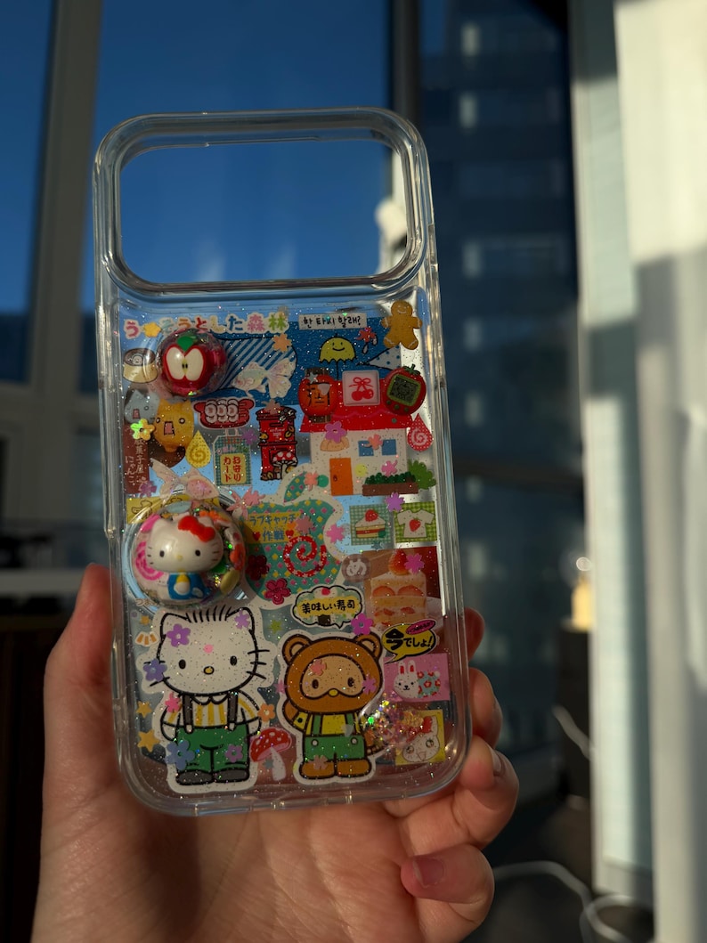Puede incluir: Funda de tel&eacute;fono transparente decorada con pegatinas y abalorios de colores. Presenta a Hello Kitty, un oso y otras ilustraciones bonitas. Incluye texto japon&eacute;s y un pop socket con dise&ntilde;o de Hello Kitty.