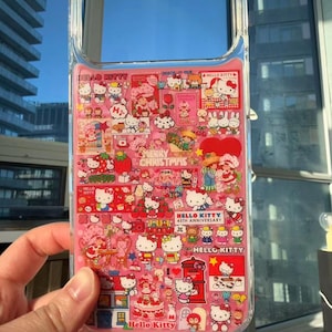 May include: Clear phone case with a pink interior featuring numerous Hello Kitty illustrations and text. The design includes various scenes with Hello Kitty, strawberries, and the text "Merry Christmas" and "Hello Kitty 45th Anniversary".