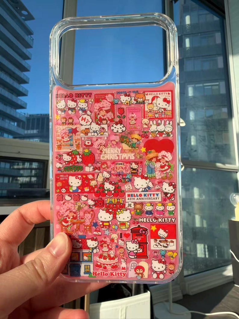 May include: Clear phone case with a pink interior featuring numerous Hello Kitty illustrations and text. The design includes various scenes with Hello Kitty, strawberries, and the text "Merry Christmas" and "Hello Kitty 45th Anniversary".