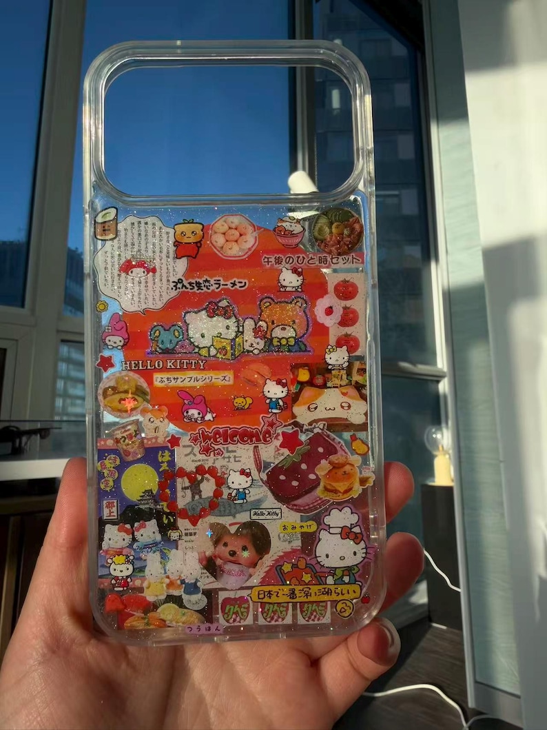 Pu&ograve; includere: Custodia trasparente per telefono con personaggi di Hello Kitty e testo giapponese. La custodia presenta immagini di Hello Kitty, cibo e altri elementi decorativi. La custodia &egrave; tenuta davanti a una finestra.
