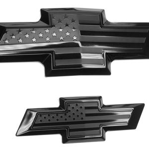 May include: Two black car emblems in the shape of a bow tie. The emblems feature a design of the American flag, with stars and stripes. The emblems are glossy and appear to be made of metal or a similar material.