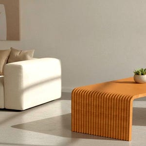 May include: A light orange coffee table with a curved, fluted design featuring vertical ridges along the side. A small, round, white ceramic pot containing a green succulent plant sits on the flat, smooth surface of the wooden coffee table.