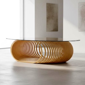 May include: A coffee table featuring a clear oval glass top resting on a base constructed from a series of light-toned wooden rings arranged in a horizontal, elongated oval formation, creating a hollow, slatted structure with an open centre.