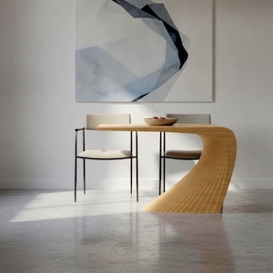 Könnte beinhalten: Ein heller Holzesstisch mit einem geschwungenen, gerippten Stützfuß, der in eine flache Tischplatte übergeht. Zwei Stühle mit dünnen schwarzen Metallrahmen und hellen Polstersitzen sind an dem Tisch positioniert.