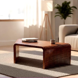 May include: A low-profile coffee table crafted from dark brown wood, featuring a smooth, flat top surface and curved, slatted sides that create a continuous, rounded silhouette. Two stacked books and a small ceramic mug sit on the table.