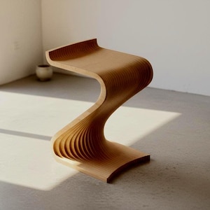 Può includere: Uno sgabello in legno marrone chiaro caratterizzato da una silhouette fluida e continua a forma di S. La struttura è composta da molteplici strati sottili di legno impilati che creano un aspetto nervato e strutturato lungo i bordi curvi.