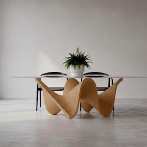 May include: A dining table with a clear glass top and a light brown, wavy, ribbed base. Two black chairs are positioned behind the table, and a green potted plant sits in a white container on the centre of the glass surface.