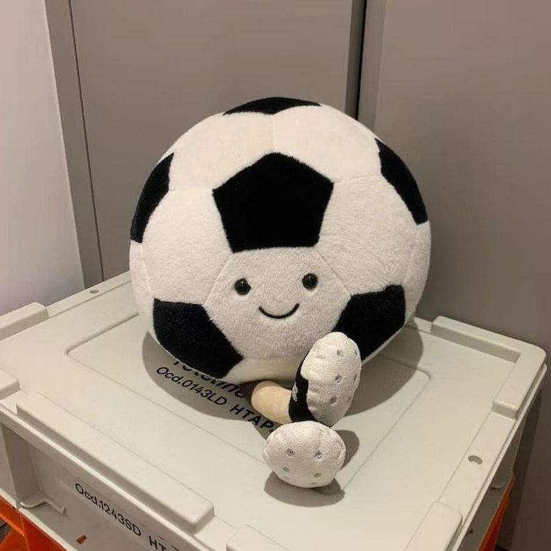 Puede incluir: Un bal&oacute;n de f&uacute;tbol de peluche en blanco y negro con una cara sonriente. Presenta un dise&ntilde;o de pent&aacute;gonos. Tambi&eacute;n hay dos piezas de peluche m&aacute;s peque&ntilde;as a juego. El juguete es suave y tierno.