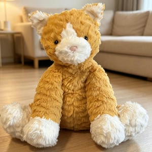 May include: A plush orange cat with white accents on its face, paws, and ears. The stuffed animal has a soft, textured appearance and is sitting upright. The cat's nose is pink, and it has black eyes.