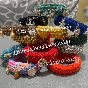 Può includere: Una collezione di braccialetti colorati fatti a mano. I braccialetti sono realizzati in materiale spesso e intrecciato in vari colori, tra cui verde acqua, nero, giallo, rosso e arancione. Ogni braccialetto presenta ciondoli unici, come conchiglie, stelle marine e cuori.