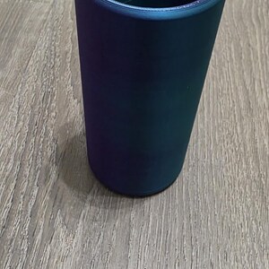 Puede incluir: Un vaso cil&iacute;ndrico con un exterior liso y s&oacute;lido que presenta un acabado de cambio de color que transita entre tonos profundos de p&uacute;rpura, azul y verde azulado. El recipiente tiene un dise&ntilde;o simple de boca abierta y una base plana.