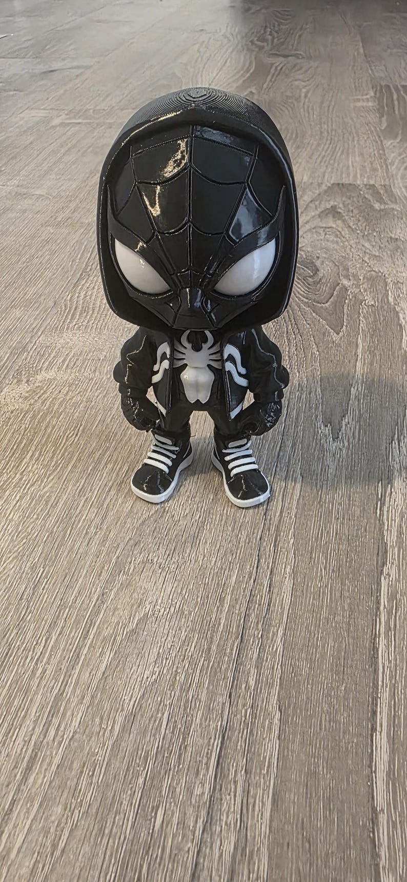 Puede incluir: Una figura Funko Pop de Spider-Man en blanco y negro. La figura lleva una sudadera con capucha y una chaqueta negras con un emblema de ara&ntilde;a blanco. Tiene ojos blancos y lleva zapatillas deportivas en blanco y negro.